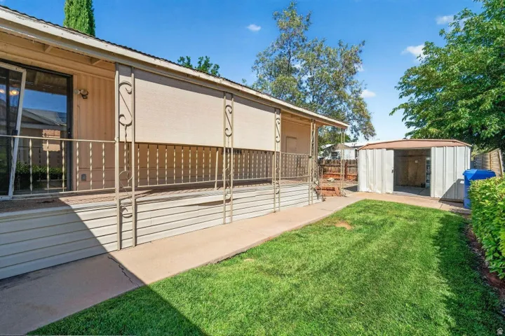Outdoor space featuring a covered porch with decorative railing, sliding glass door access, a manicured lawn, and a metal storage shed