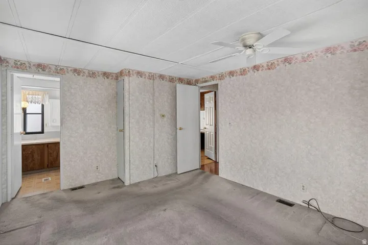 Carpeted room featuring a ceiling fan, two closet doors with brass-toned hardware, and textured wallpaper