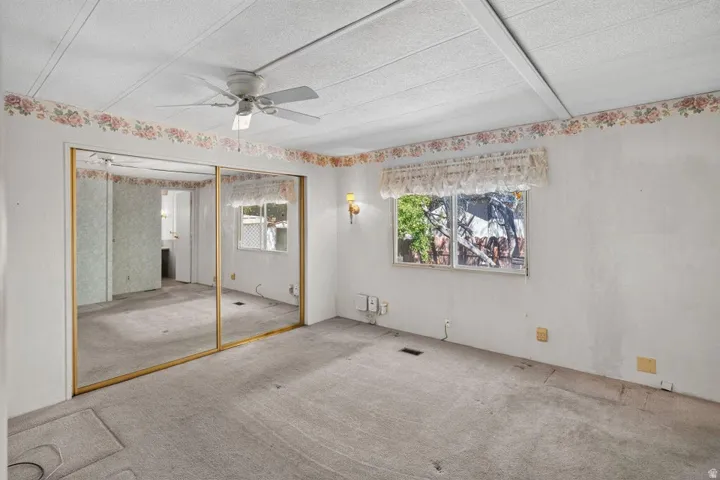 Room featuring a ceiling fan, mirrored closet doors, and a window with a valance