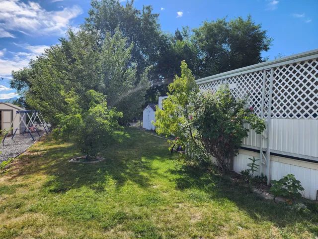 Spacious outdoor area featuring mature trees, a manicured lawn, and a white lattice privacy screen