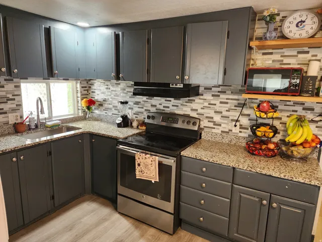 Kitchen featuring gray cabinetry, granite-look countertops, a mosaic tile backsplash, stainless steel range, and wood-finish flooring