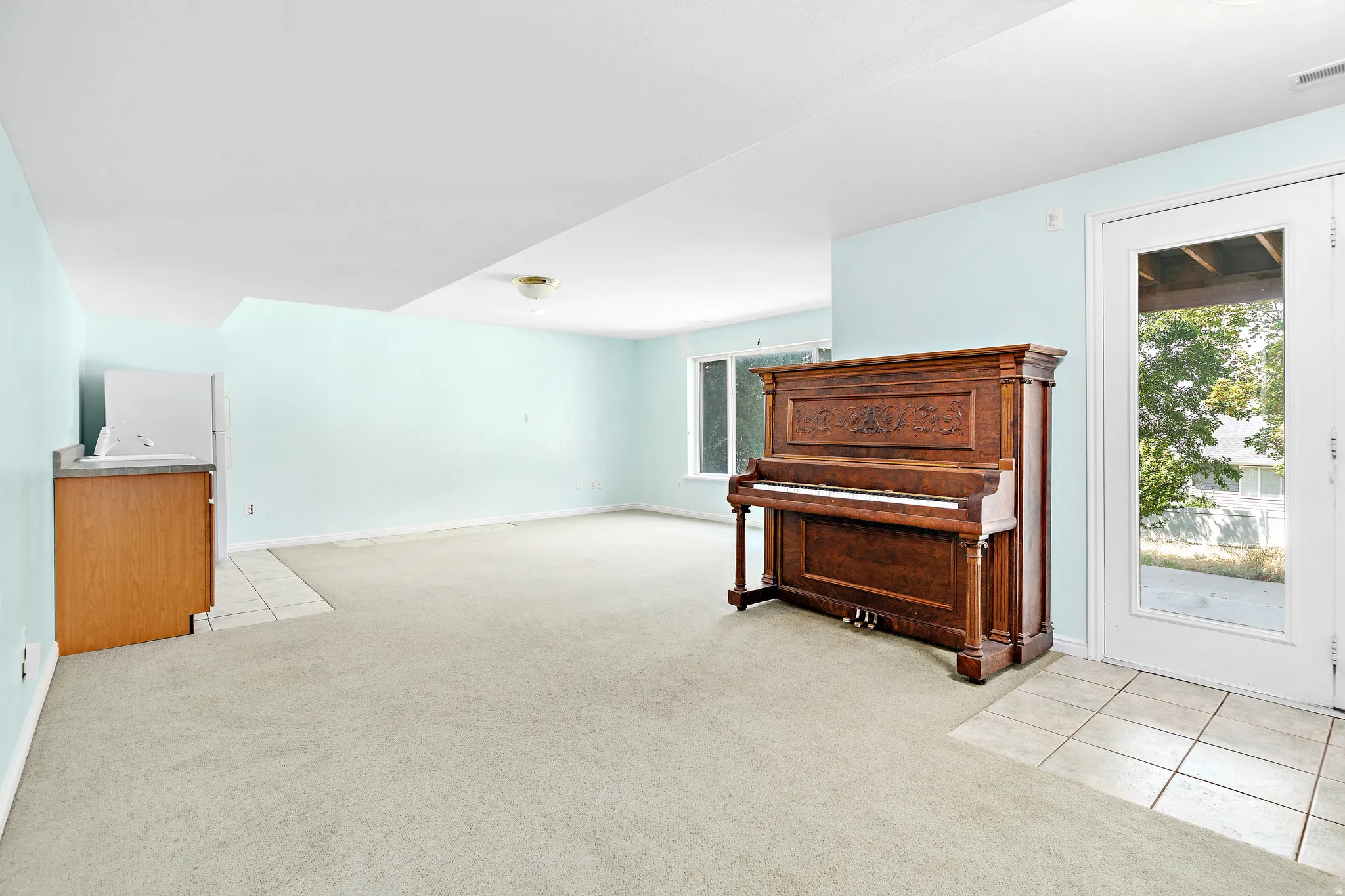 Spacious room featuring light blue walls, light-colored carpeting, and a built-in wet bar with wood cabinetry and a light-toned countertop