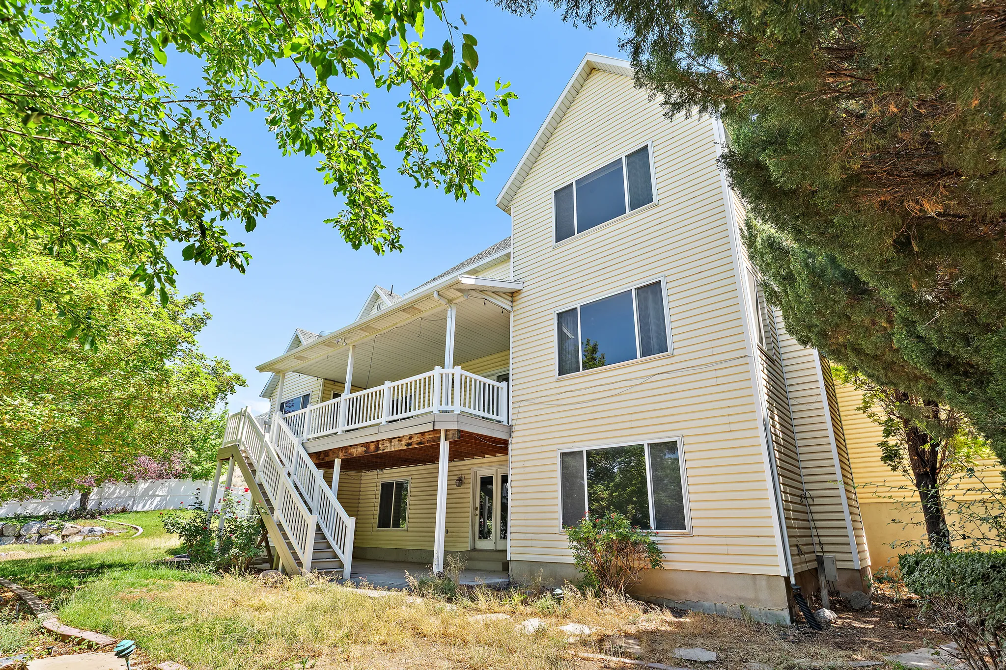 Multi-level residence featuring light-colored siding, multiple windows, a covered upper-level deck with white railings, and an exterior staircase