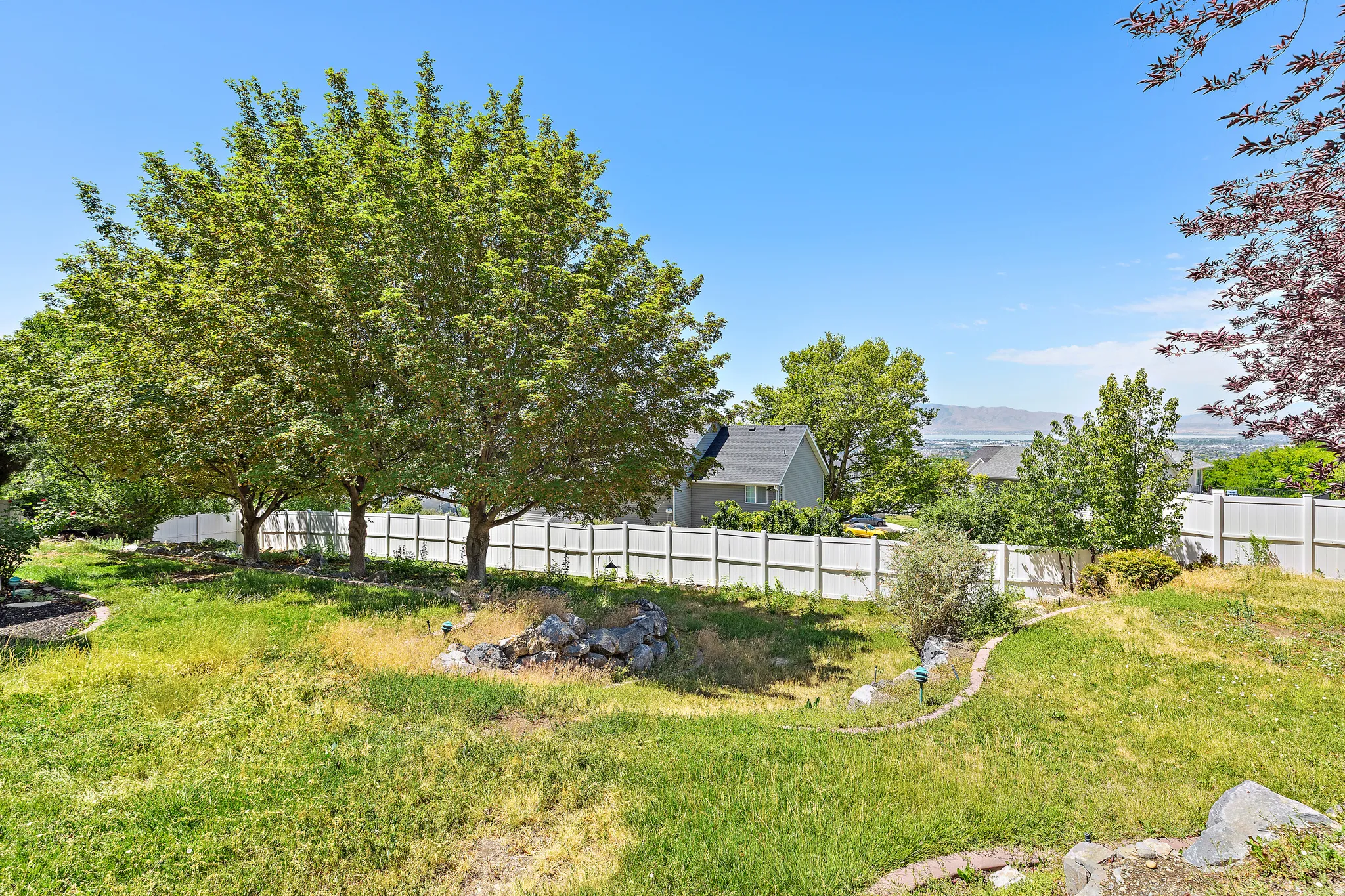 Spacious outdoor area featuring mature trees, a white perimeter fence, and a distant mountain range