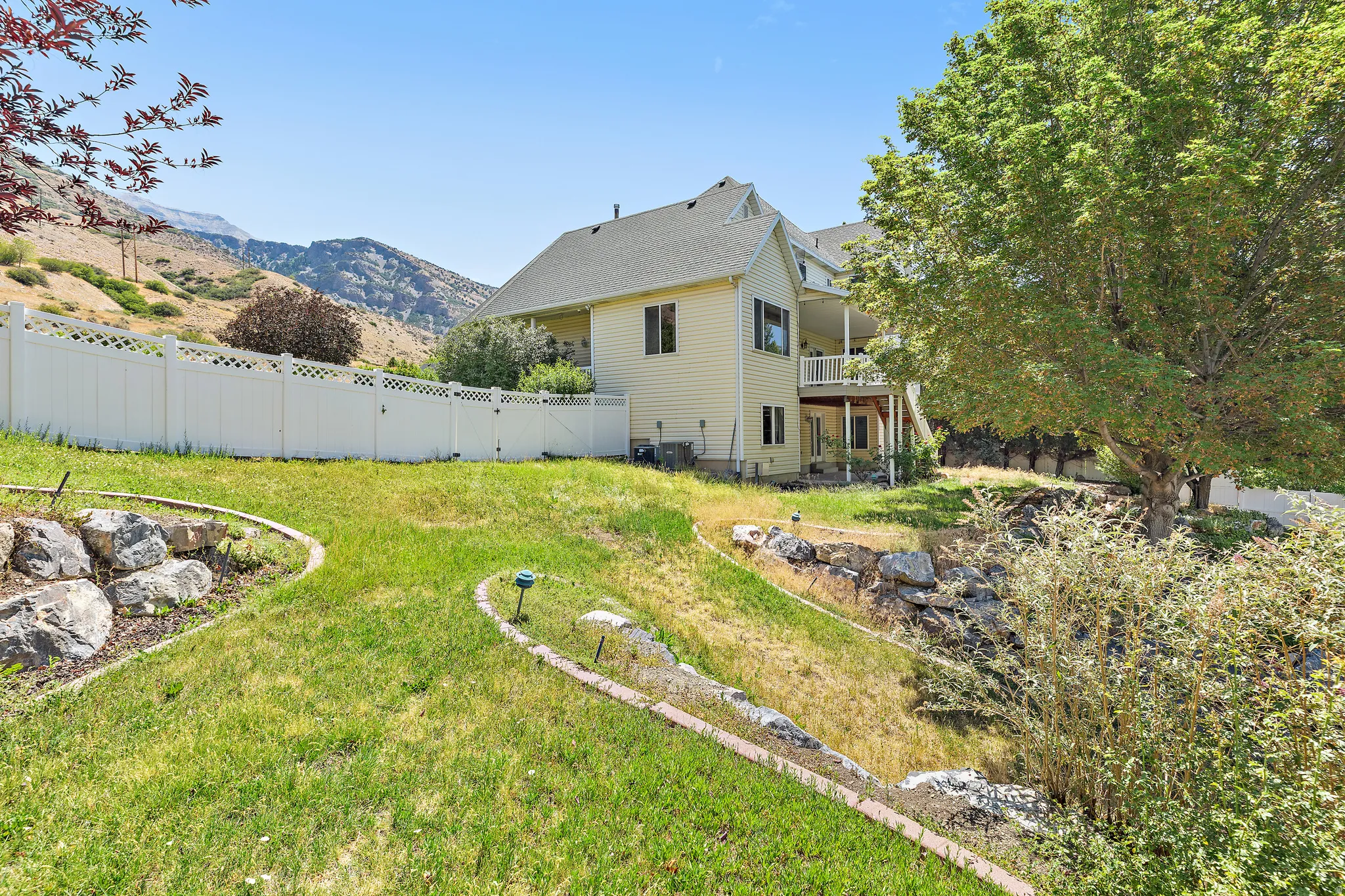 Expansive terraced backyard featuring a vinyl privacy fence, mature trees, and natural rock landscaping
