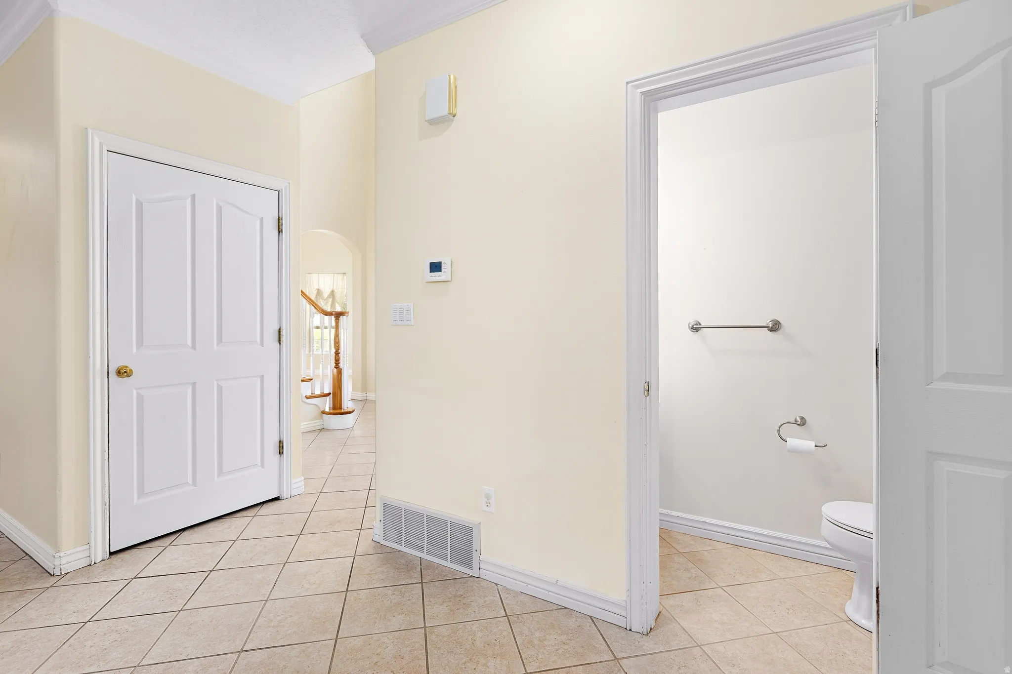 Tiled flooring in a neutral tone, crown molding, a white paneled door, and a thermostat