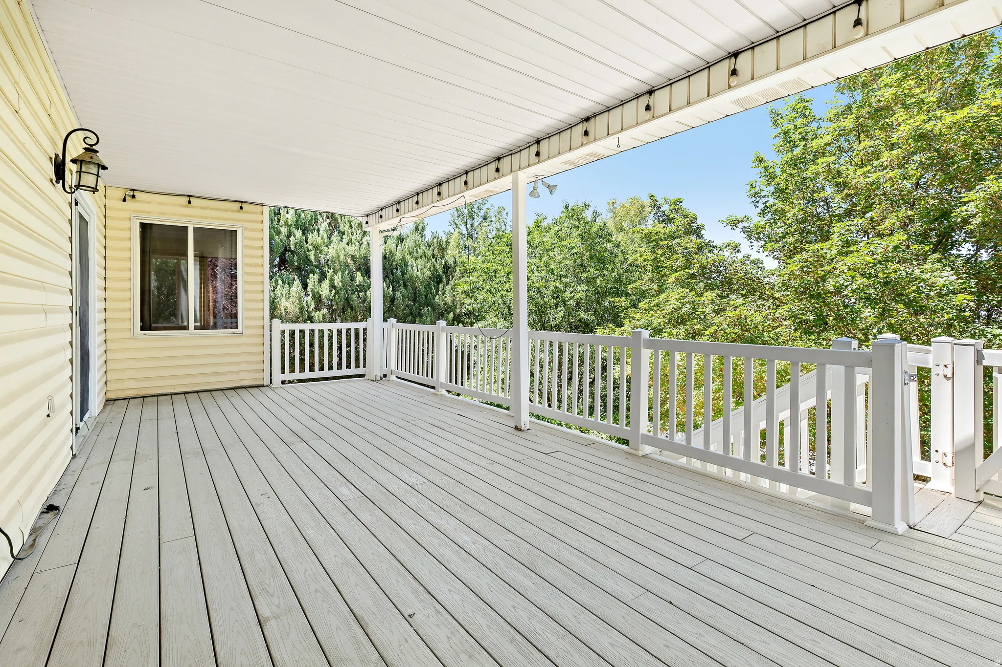 Spacious covered deck featuring composite decking, white railing, and exterior wall lighting