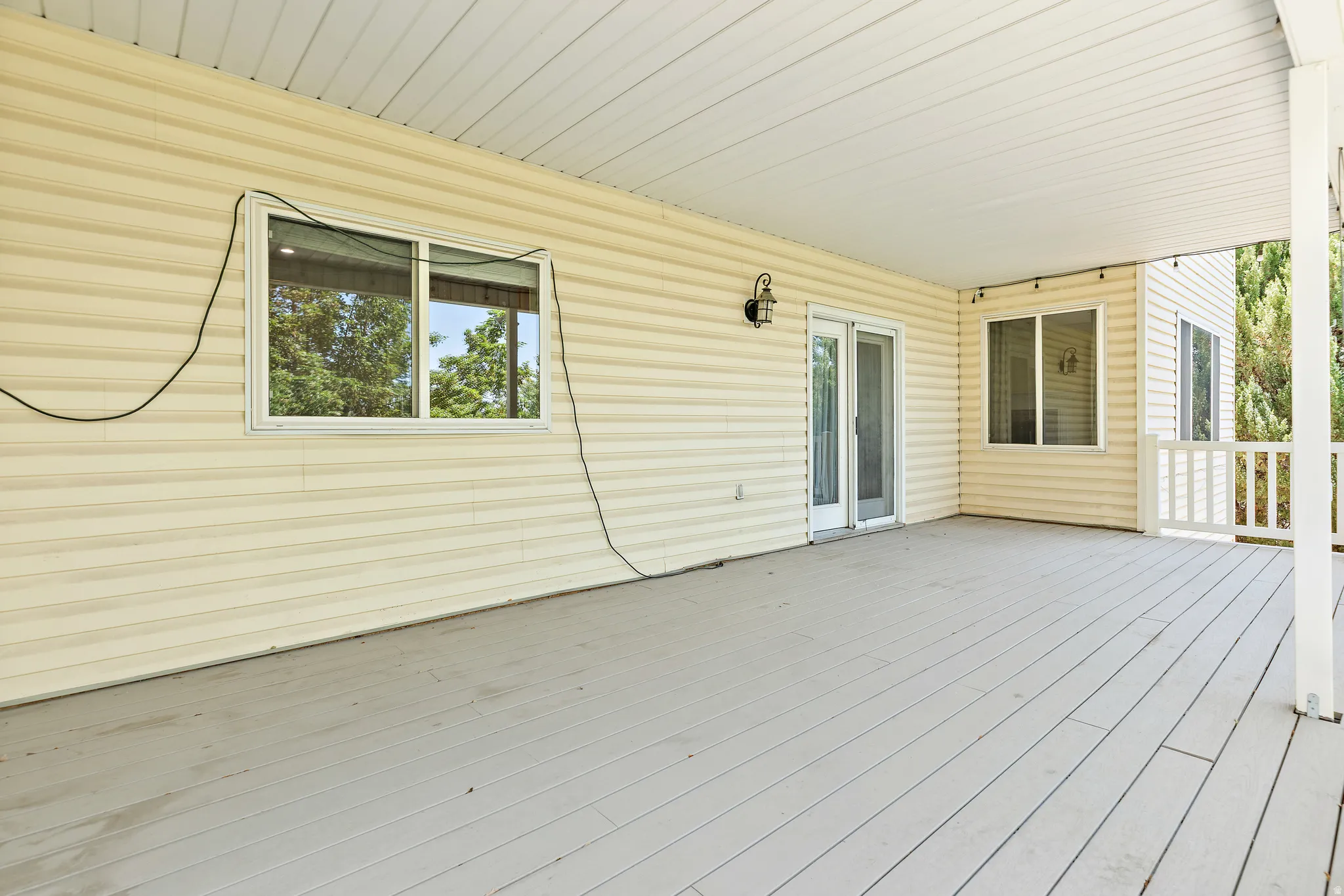 Expansive covered deck featuring a light gray wood-finish floor, white ceiling, and white siding
