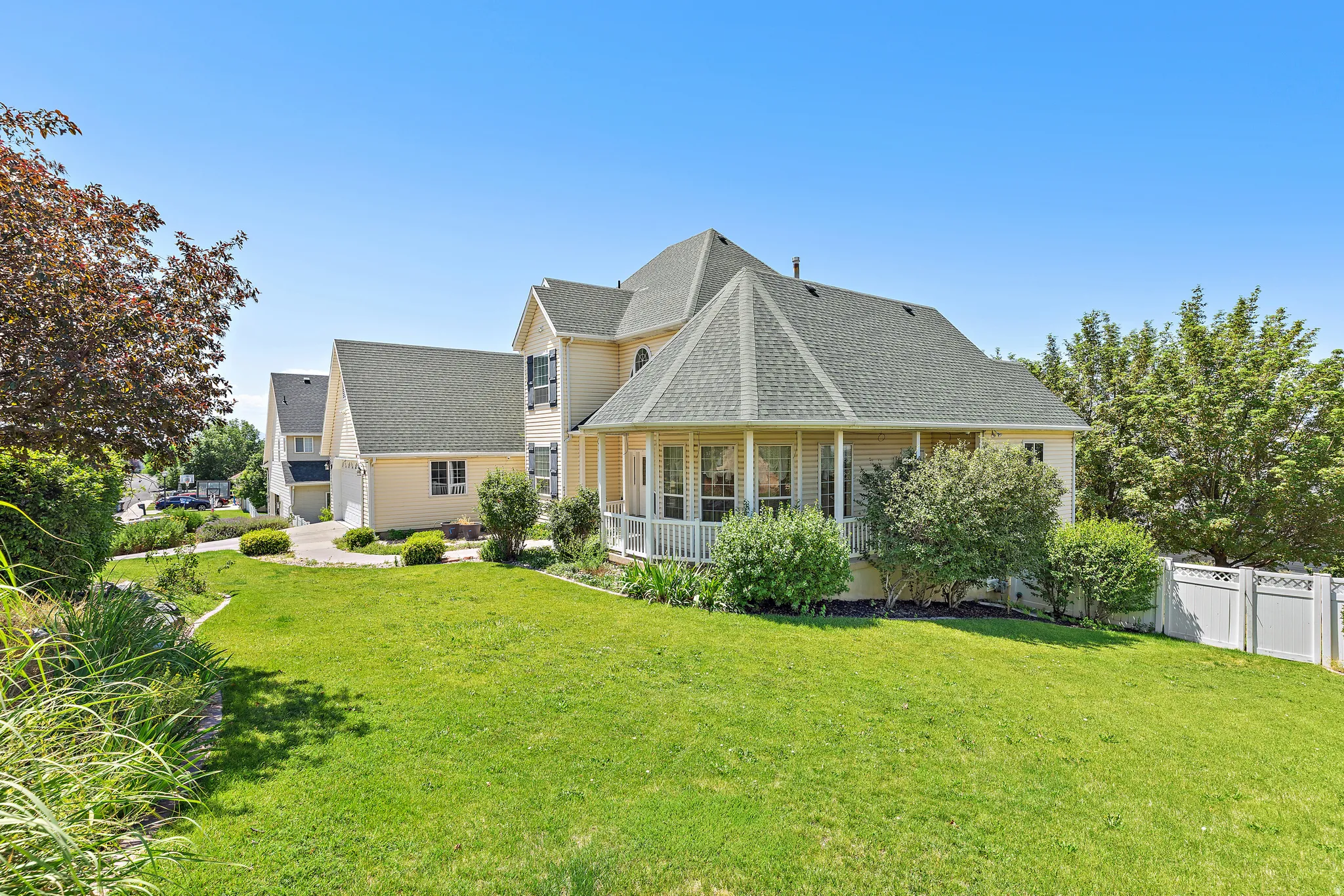 Expansive green lawn with mature landscaping, featuring a two-story residence with a screened porch and attached garage