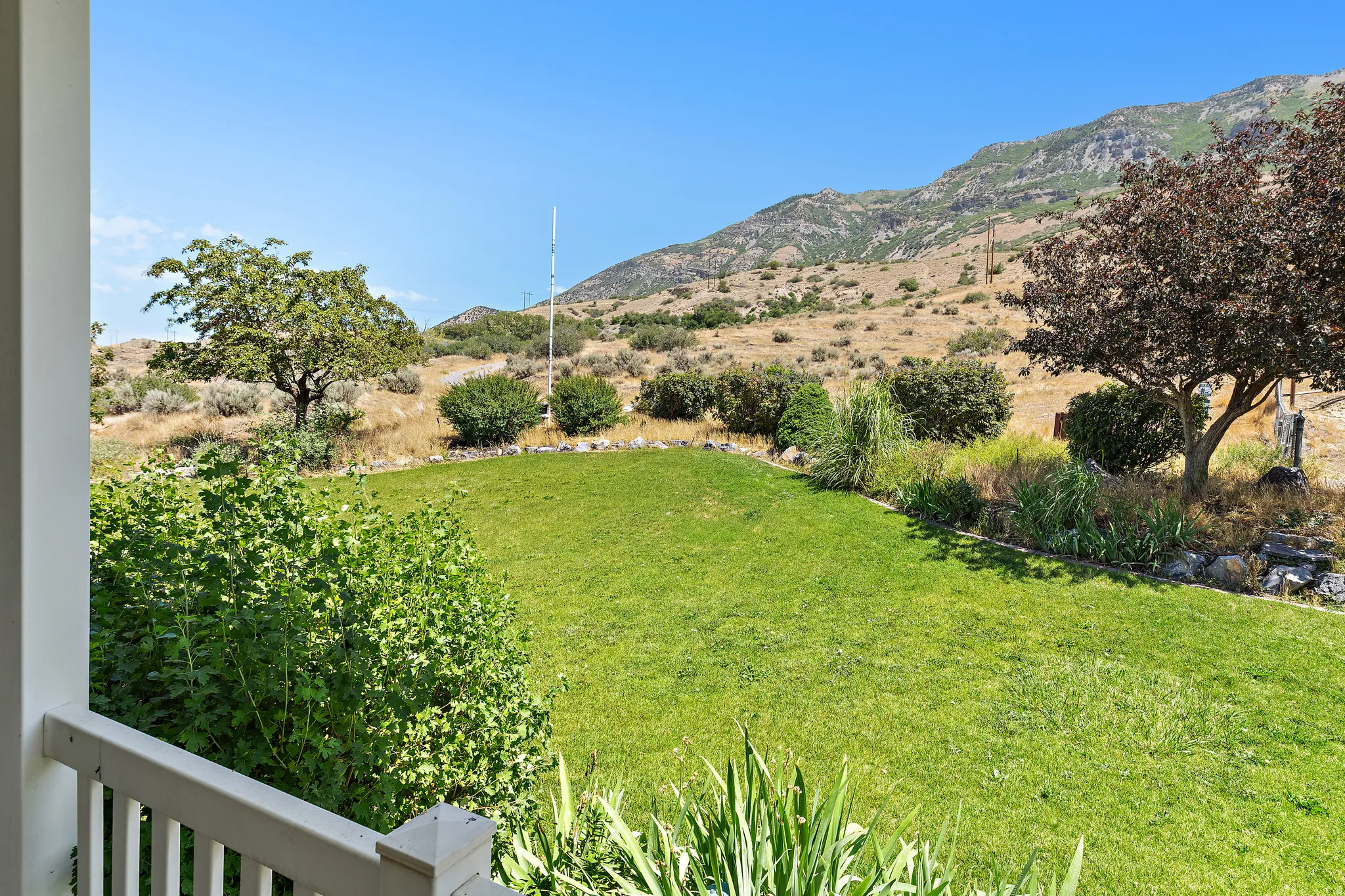 Expansive green lawn framed by a white railing, featuring mature trees and established landscaping