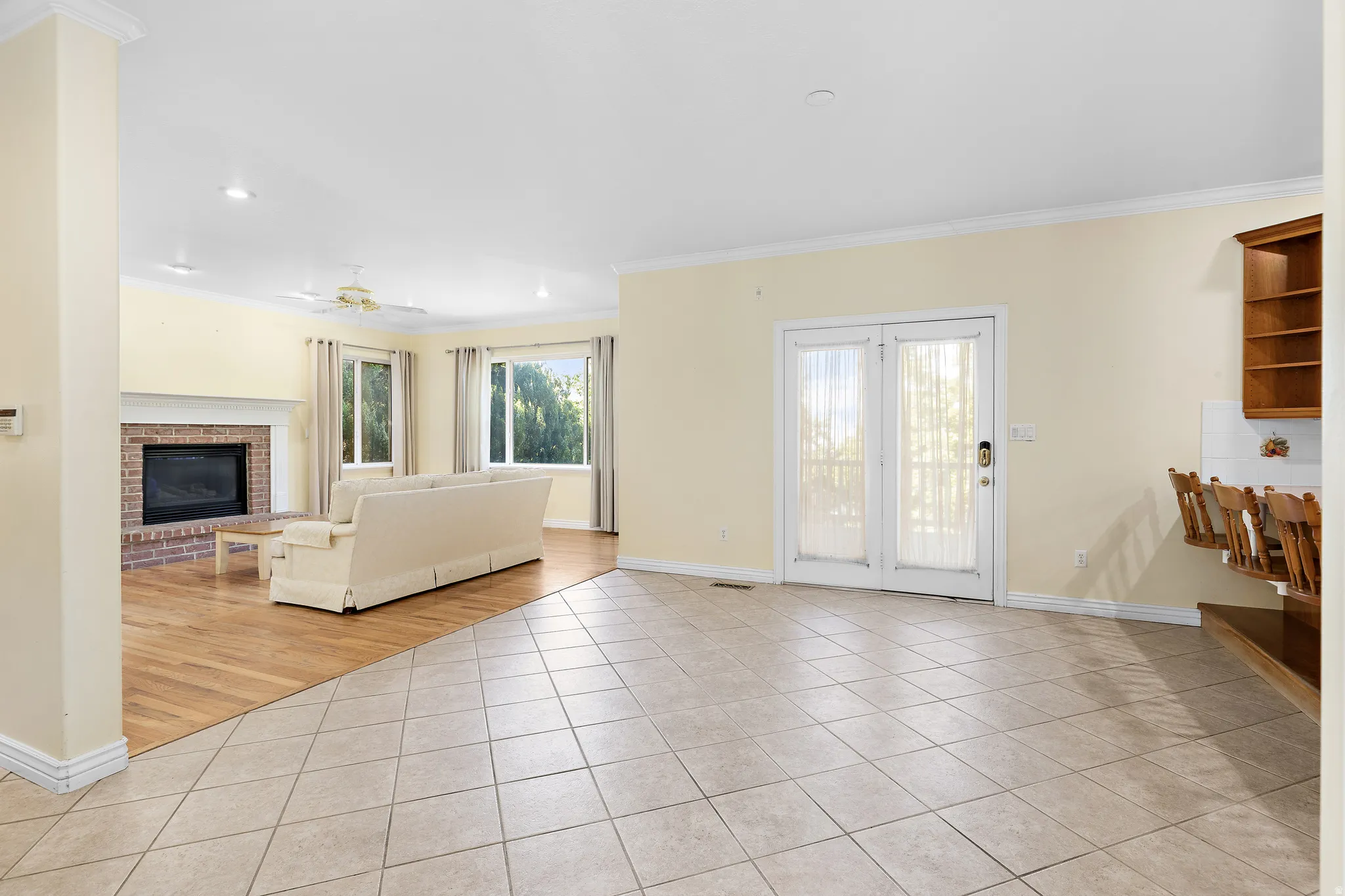 Expansive living space featuring a brick fireplace with a white mantel, wood-finish flooring, and multiple windows