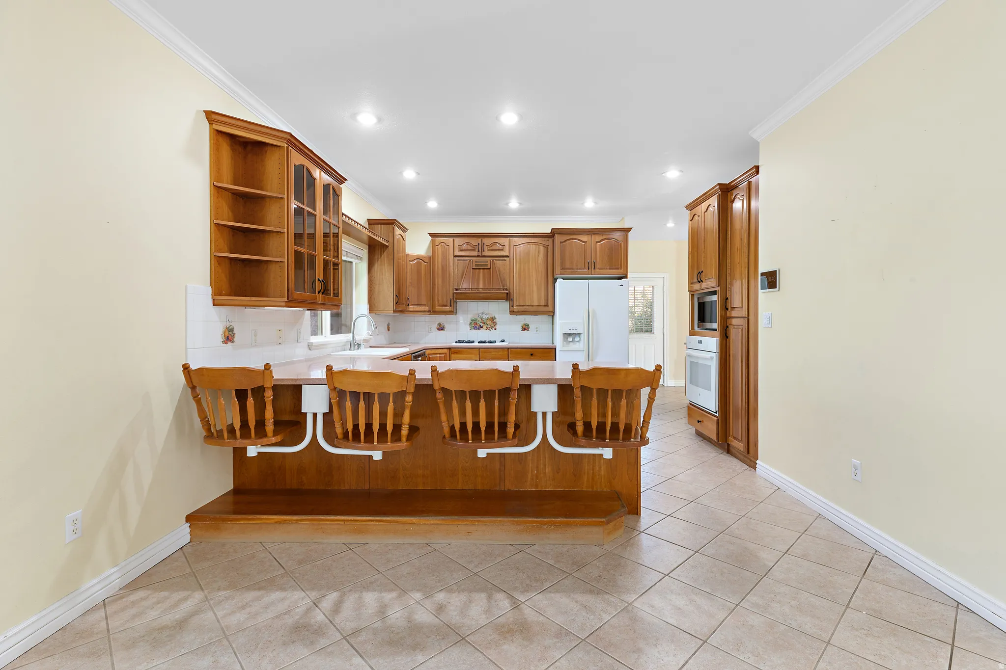Open-concept kitchen featuring wood cabinetry, recessed lighting, a breakfast bar with built-in seating, a double-door refrigerator, and tile flooring