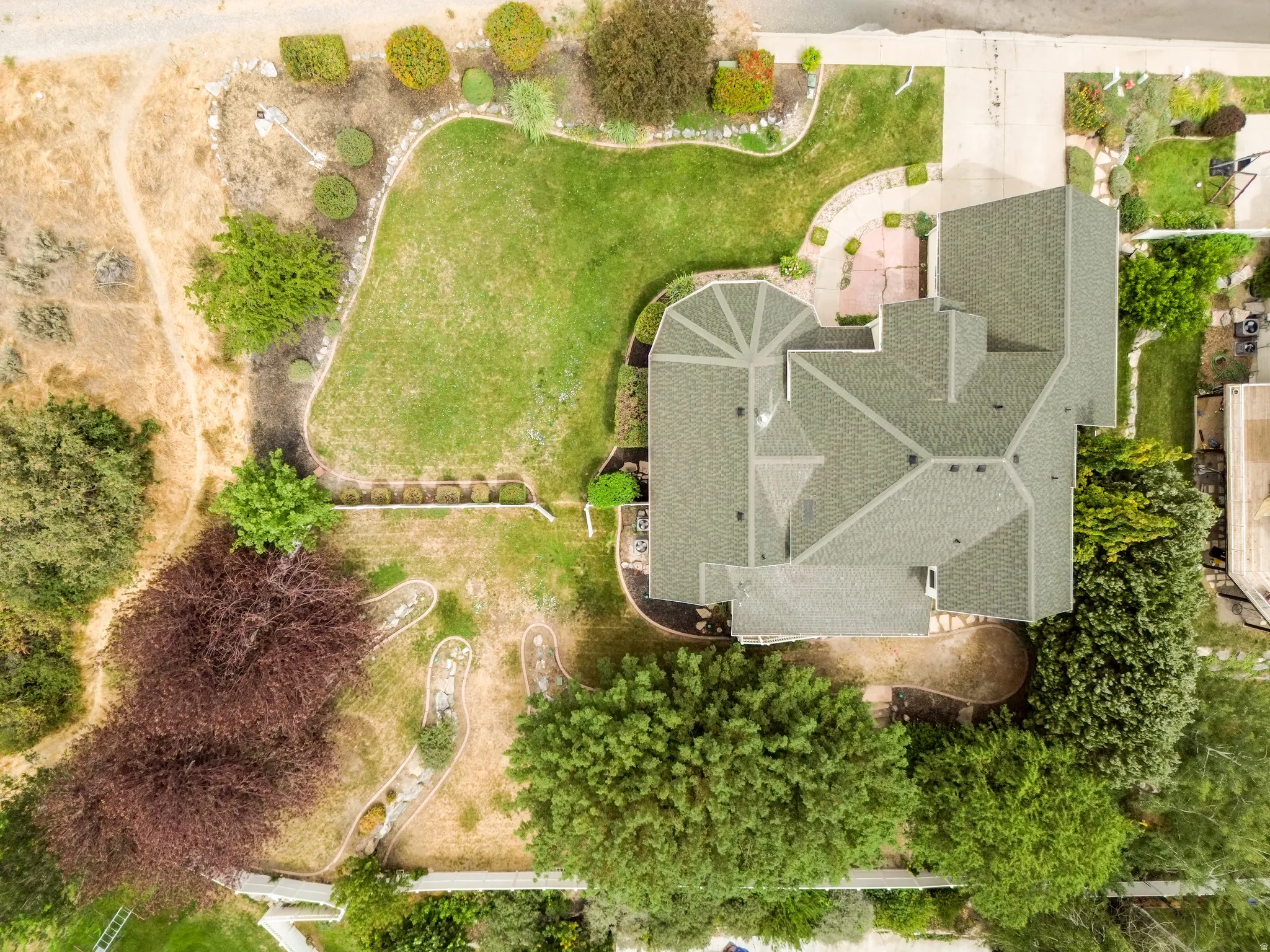 Expansive property featuring a multi-gabled roofline, varied landscaping elements, a paved driveway, and mature trees
