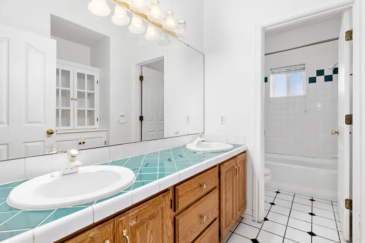 Double vanity with wood cabinetry, featuring a large mirror and overhead multi-bulb lighting