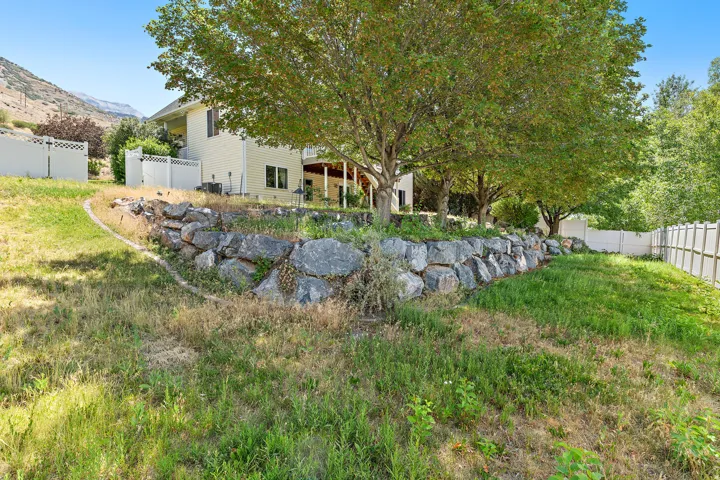 Rear exterior featuring a stone retaining wall, mature trees, and a private balcony