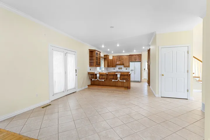 Spacious open-concept area featuring diagonal tile flooring, a kitchen with wood cabinetry and recessed lighting, and white French doors