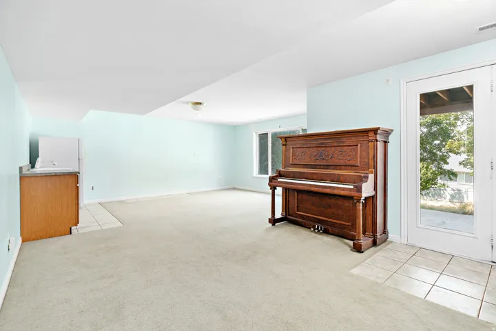Spacious room featuring light blue walls, light-colored carpeting, and a built-in wet bar with wood cabinetry and a light-toned countertop