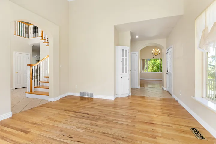 Bright interior featuring hardwood flooring, arched doorways, a built-in corner cabinet, a window with exterior visibility, and a visible staircase with wood newel posts and handrails