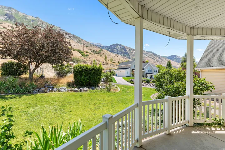 Covered concrete patio with white railing overlooking a sloped grass lawn