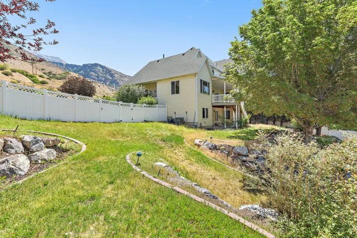 Expansive terraced backyard featuring a vinyl privacy fence, mature trees, and natural rock landscaping