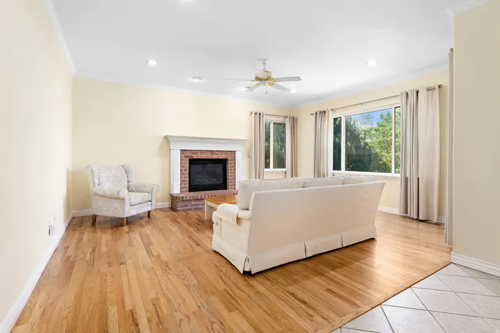 Living area featuring wood-finish flooring, a brick fireplace with a white mantel, multiple windows, recessed lighting, and a ceiling fan