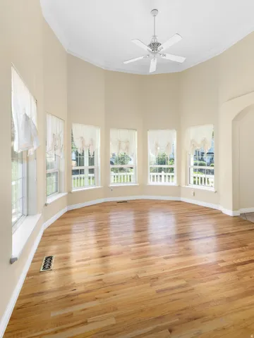 Curved window wall with multiple panels, wood-finish flooring, and a ceiling fan with integrated lighting