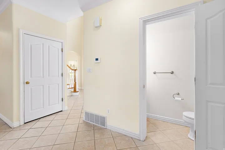 Tiled flooring in a neutral tone, crown molding, a white paneled door, and a thermostat