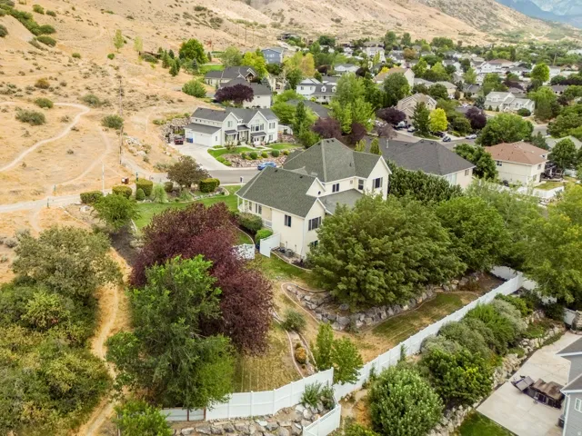 Two-story residence with a green shingle roof, surrounded by mature trees and landscaping