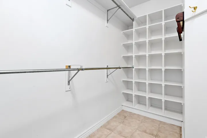 Walk-in closet featuring extensive built-in shelving, a metal hanging rod, and neutral tile flooring