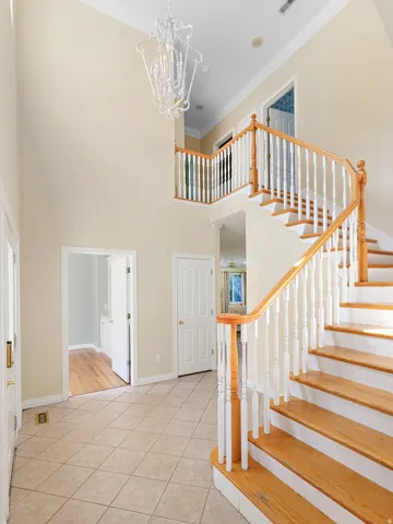 Two-story foyer featuring a grand staircase with wood treads and white balusters, ceramic tile flooring, and a decorative chandelier