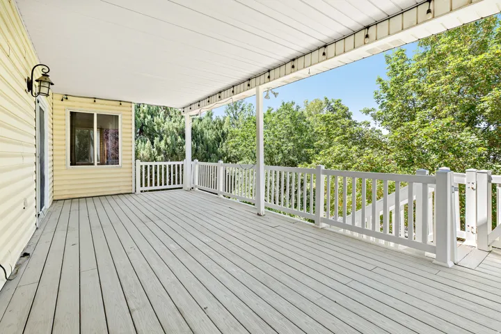 Spacious covered deck featuring composite decking, white railing, and exterior wall lighting