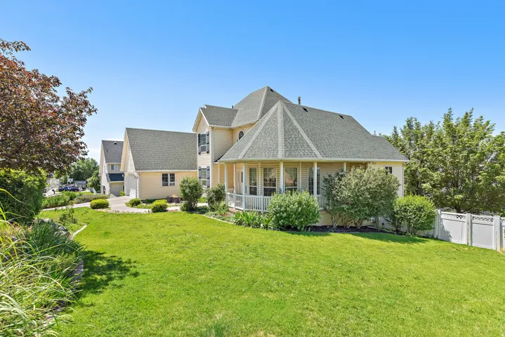 Expansive green lawn with mature landscaping, featuring a two-story residence with a screened porch and attached garage