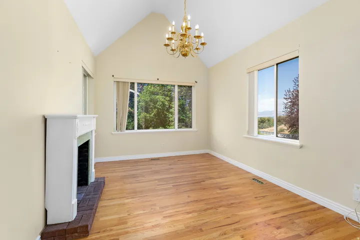Vaulted ceiling living space featuring wood-finish flooring, a white mantel fireplace with brick hearth, and multiple windows