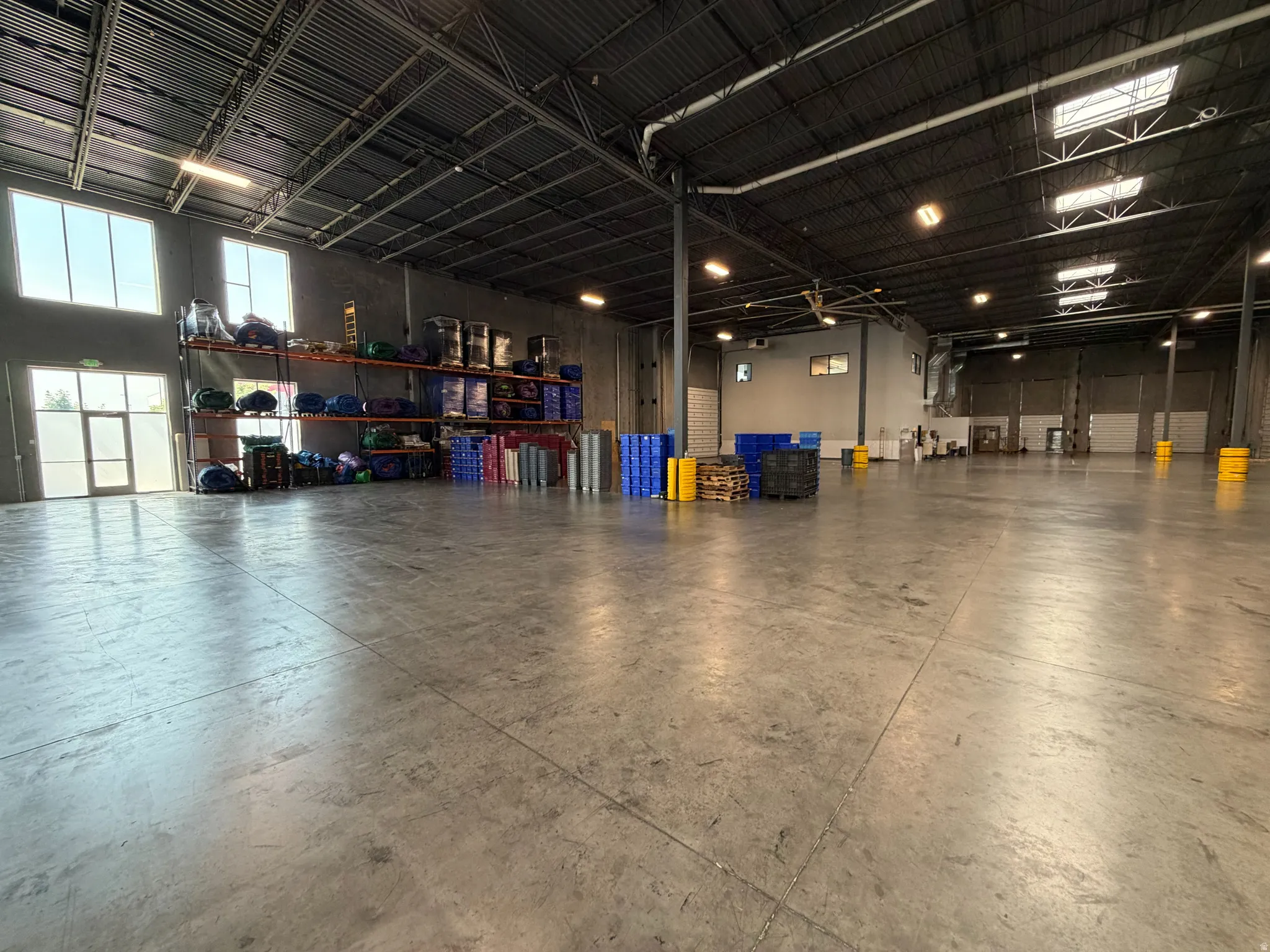 Spacious industrial interior featuring concrete flooring, high ceilings with exposed structural elements, and transom windows providing ambient light