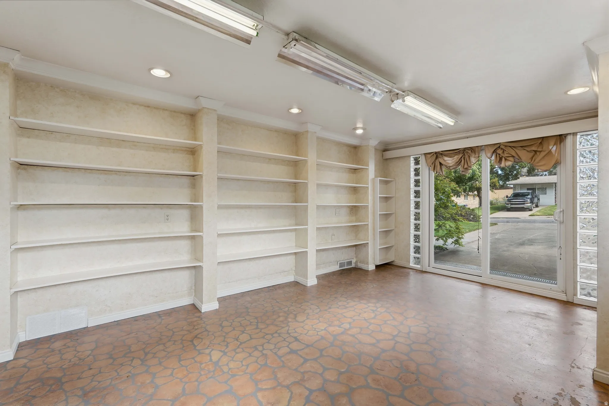 Spacious room featuring multiple built-in shelving units, recessed lighting, and dual fluorescent light fixtures