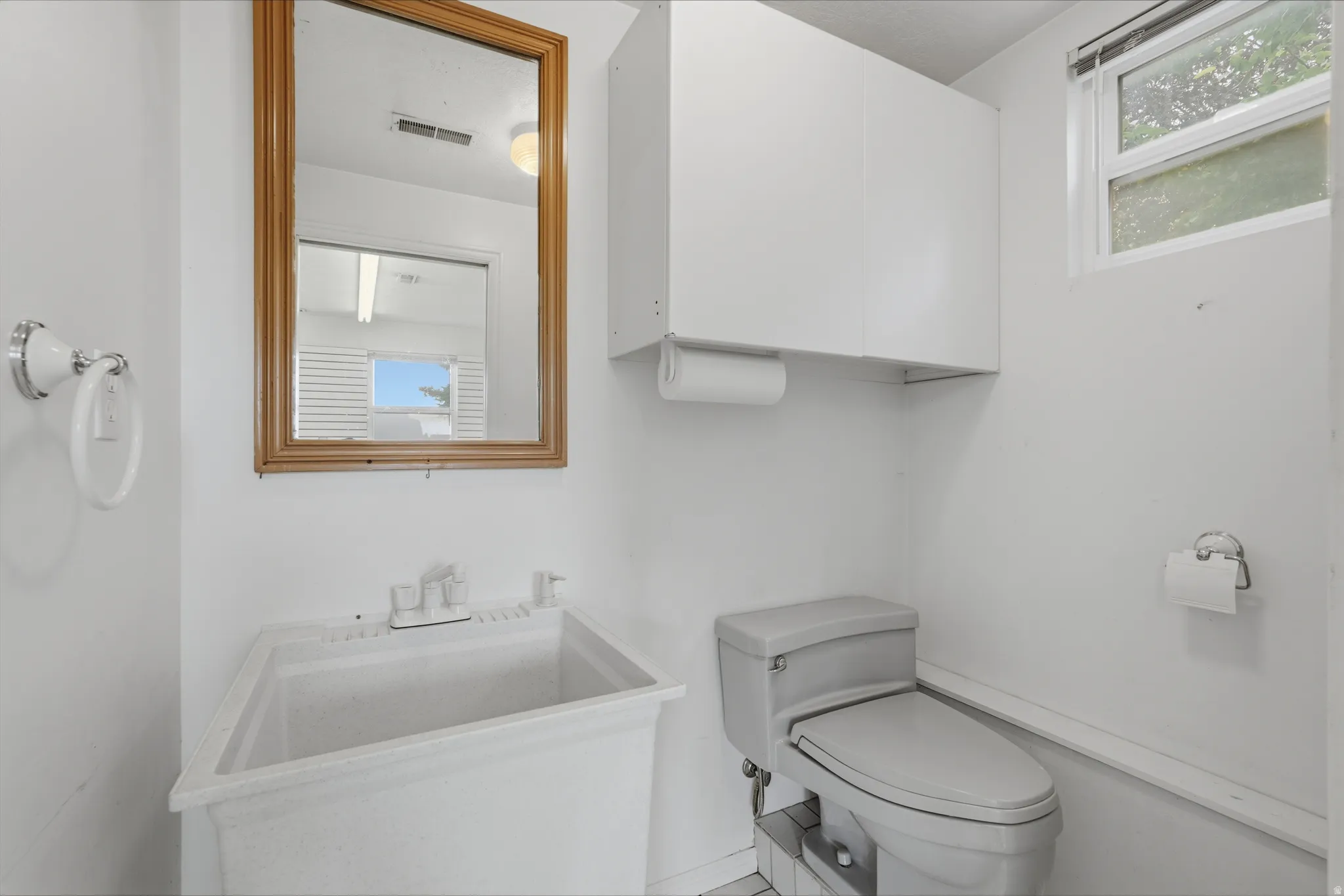 Utility room featuring a built-in basin sink, window, wall-mounted cabinetry, and a toilet