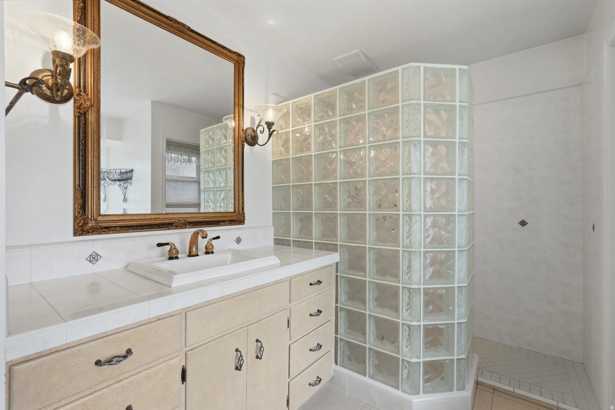 Bathroom vanity with an ornate framed mirror, dual sconce lighting, an undermount sink, and a tiled countertop