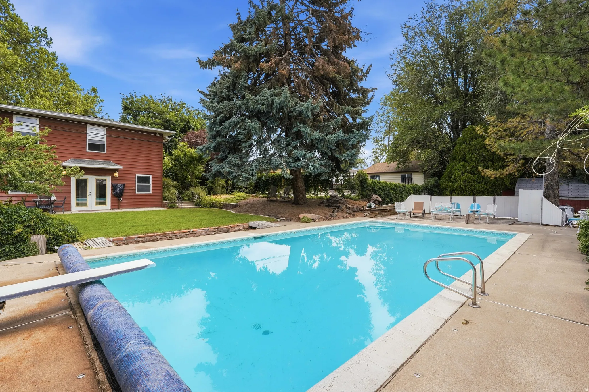 Outdoor swimming pool with concrete surround, diving board, and integrated entry steps