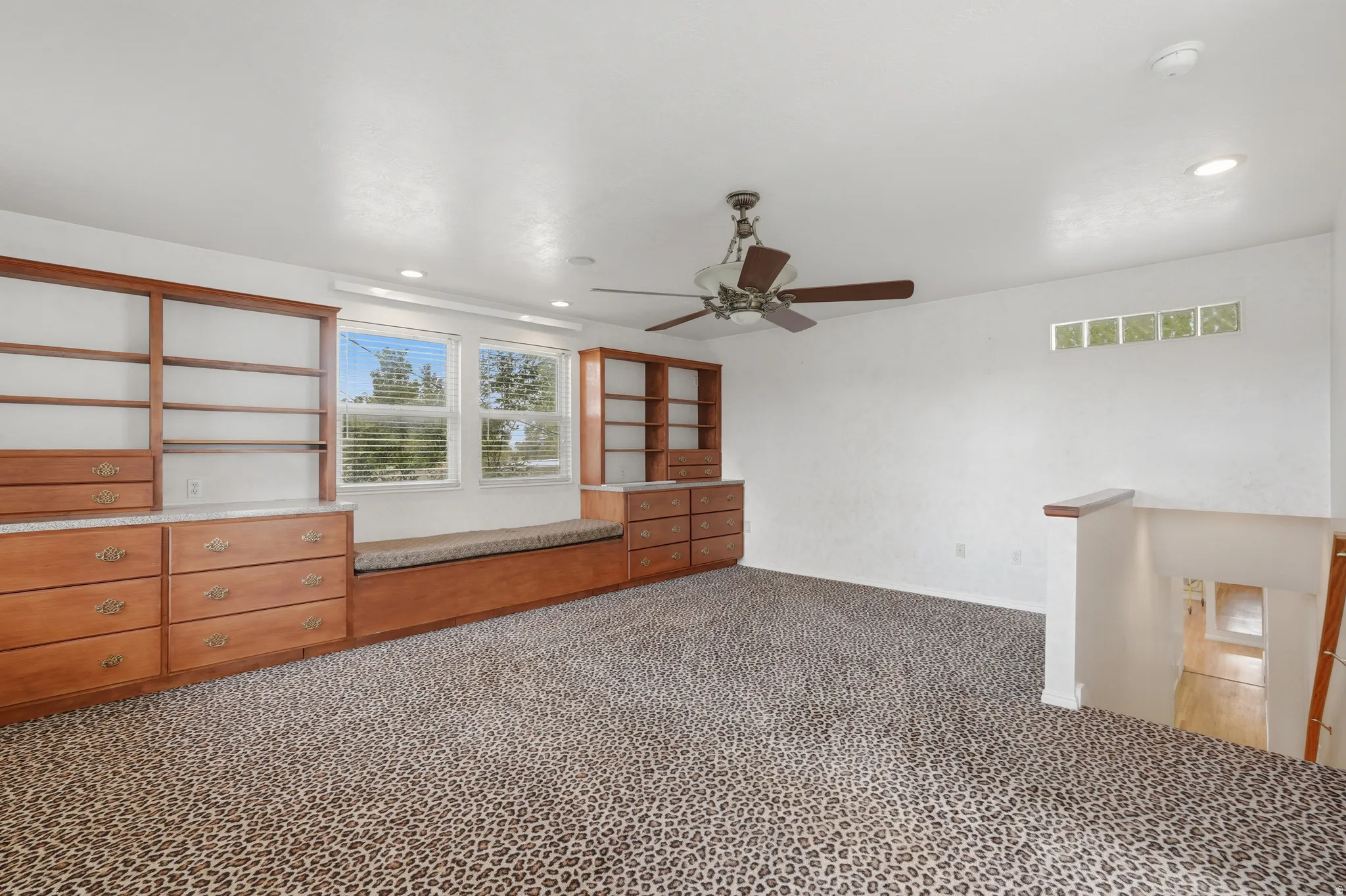 Built-in wood cabinetry with shelving and drawers, window seating with cushion, dual windows with blinds, recessed lighting, and a ceiling fan