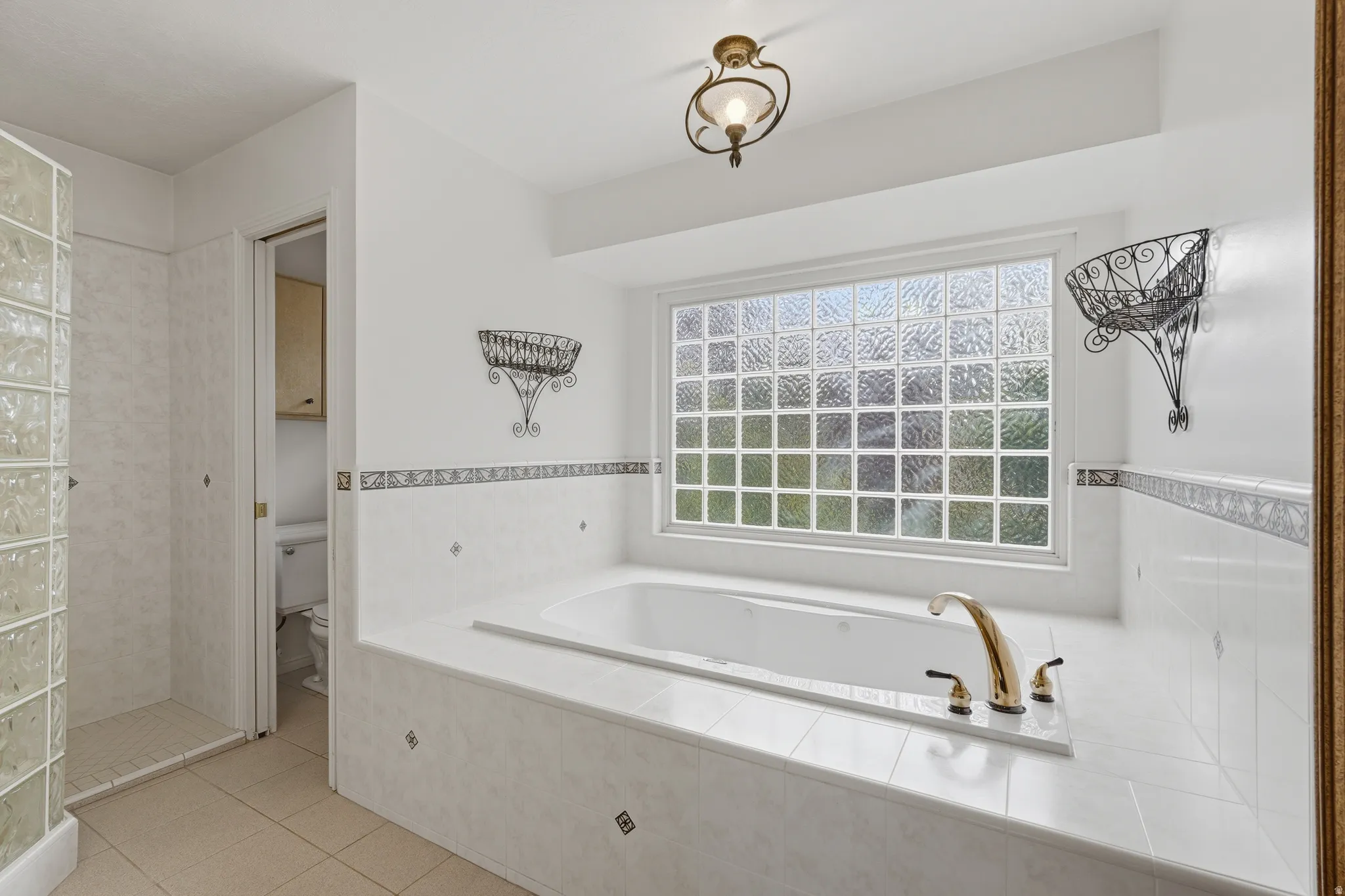 Spacious bath featuring an oversized soaking tub with brass fixtures, a large glass block window, and a separate glass block shower enclosure