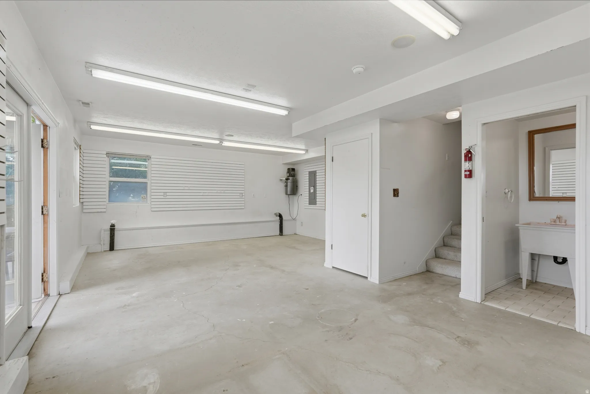 Spacious utility area featuring concrete flooring, multiple fluorescent light fixtures, and white walls