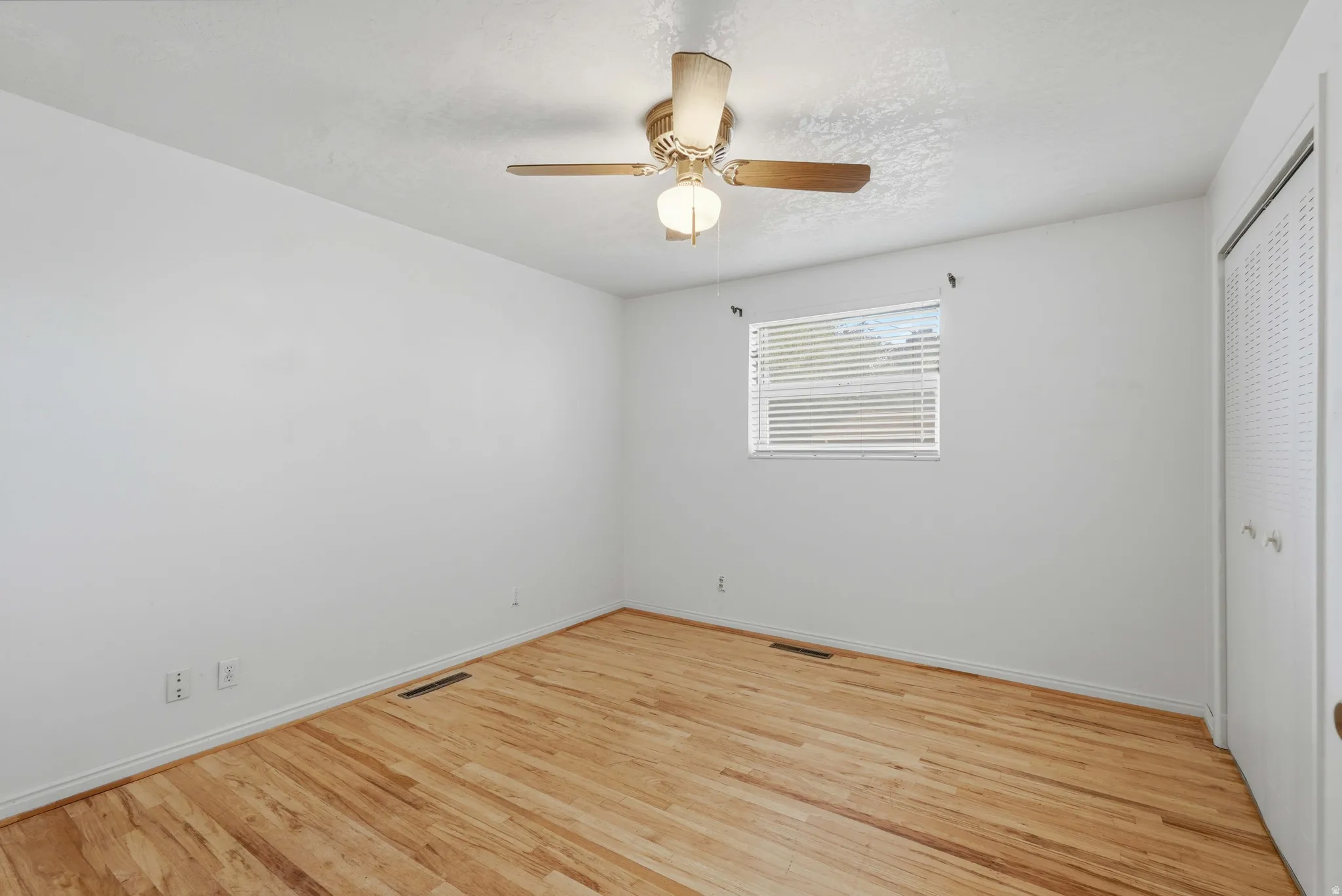 Bright room featuring wood-finish flooring, white walls, and a ceiling fan with integrated lighting