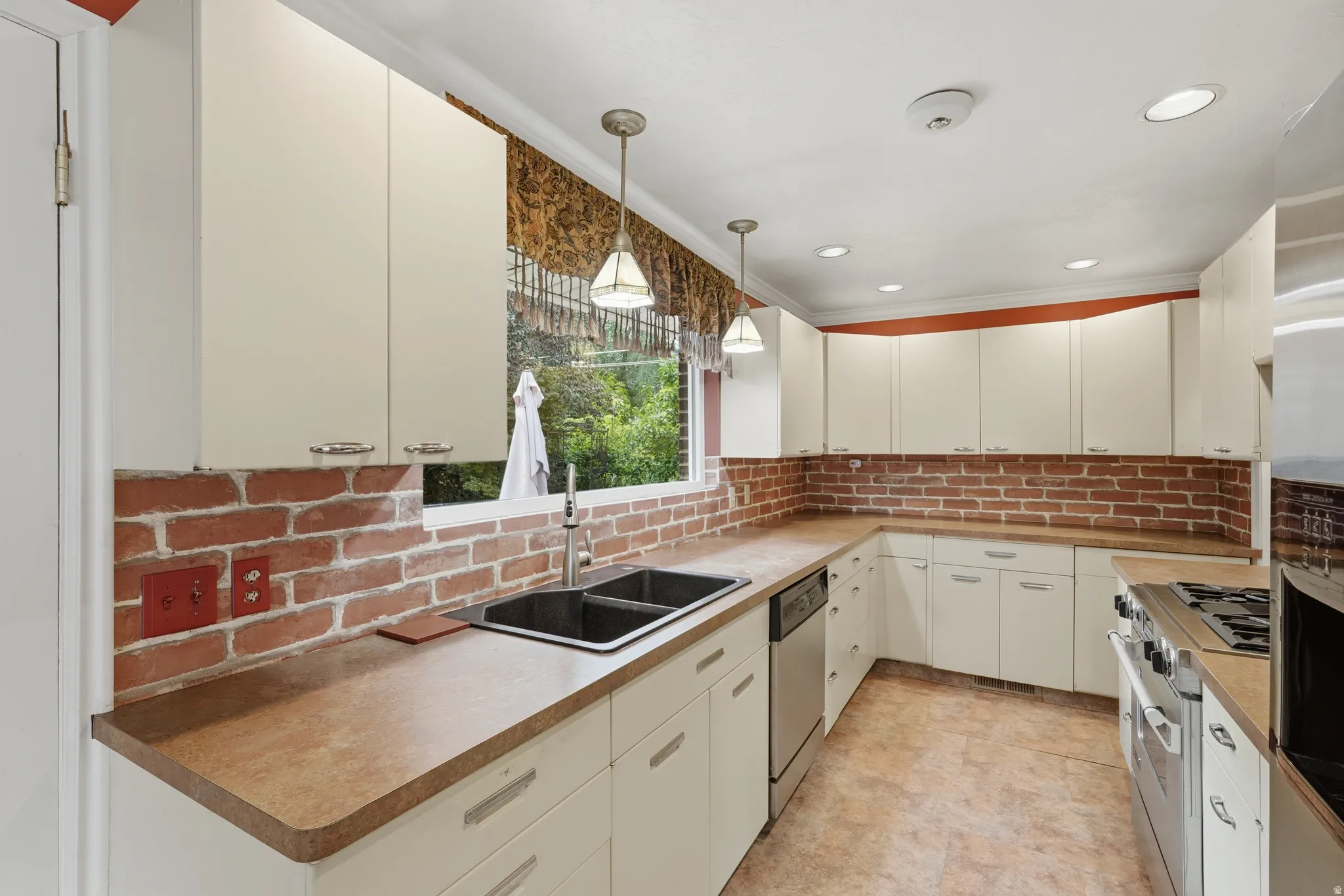 U-shaped kitchen featuring white cabinetry, brick backsplash, and a double basin sink