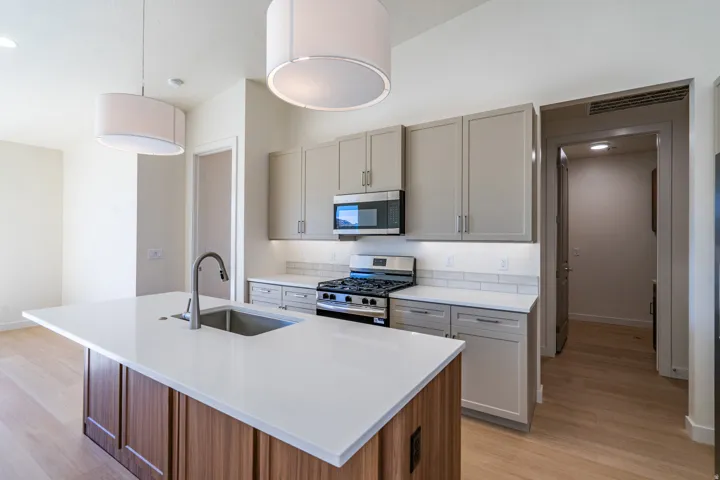 Kitchen with stainless steel appliances, a kitchen island with sink, light wood-style floors, light stone countertops, and two tone cabinetry