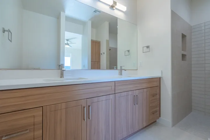 Bathroom with double vanity, ceiling fan, and tiled shower