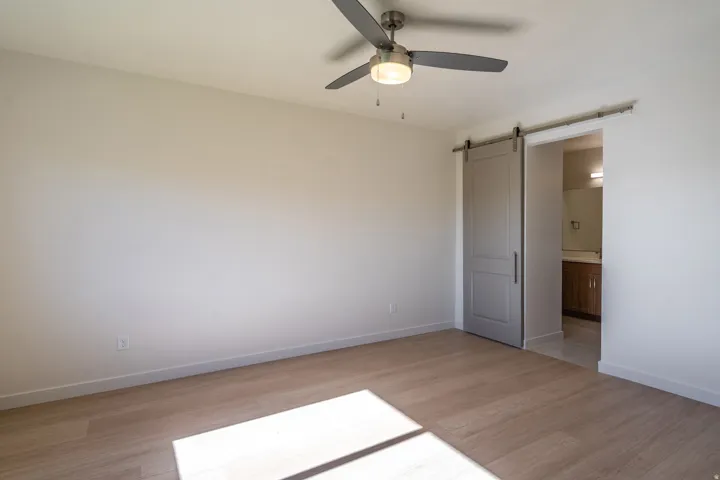 Unfurnished bedroom with a barn door, light wood-style flooring, a ceiling fan, and connected bathroom