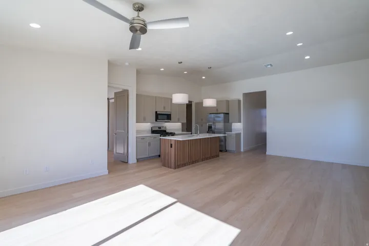 Kitchen with open floor plan, light wood finished floors, a center island with sink, hanging light fixtures, and vaulted ceiling