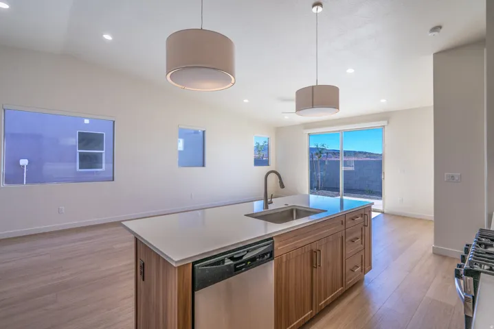 Kitchen featuring an island with sink, stainless steel appliances, light wood-style floors, decorative light fixtures, and lofted ceiling