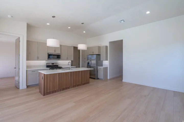 Kitchen with an island with sink, hanging light fixtures, stainless steel appliances, light wood-style flooring, and vaulted ceiling