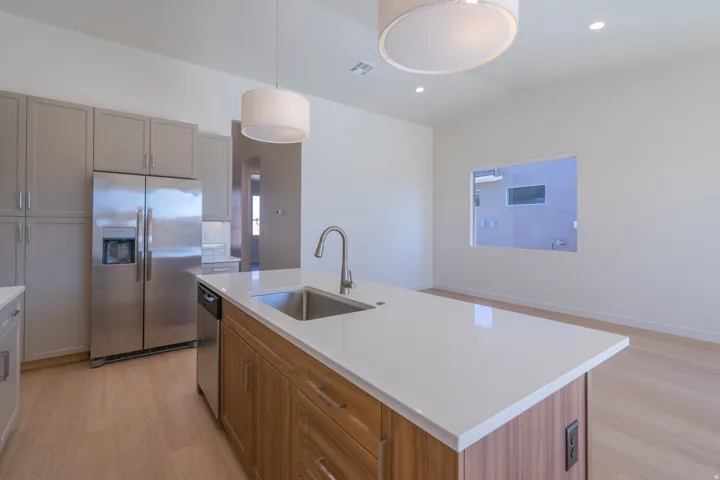 Kitchen with stainless steel appliances, light wood-style floors, vaulted ceiling, an island with sink, and decorative light fixtures